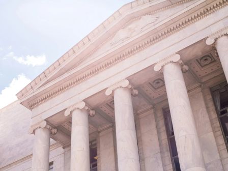 A neoclassical building with tall columns and a pediment under a bright sky.