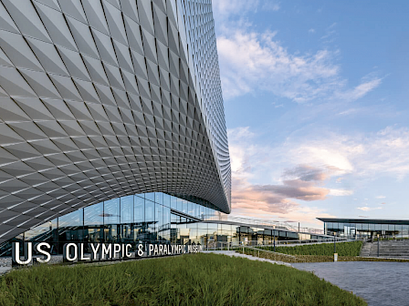 The image shows the exterior of the US Olympic & Paralympic Museum with modern architecture and clear skies.