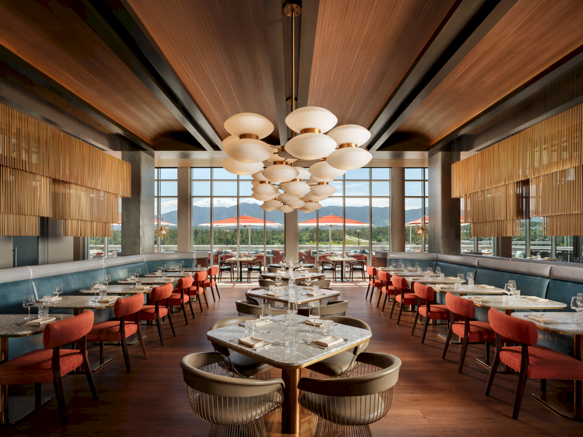 The image shows a modern restaurant interior with elegant lighting, large windows, and neatly arranged tables and chairs.