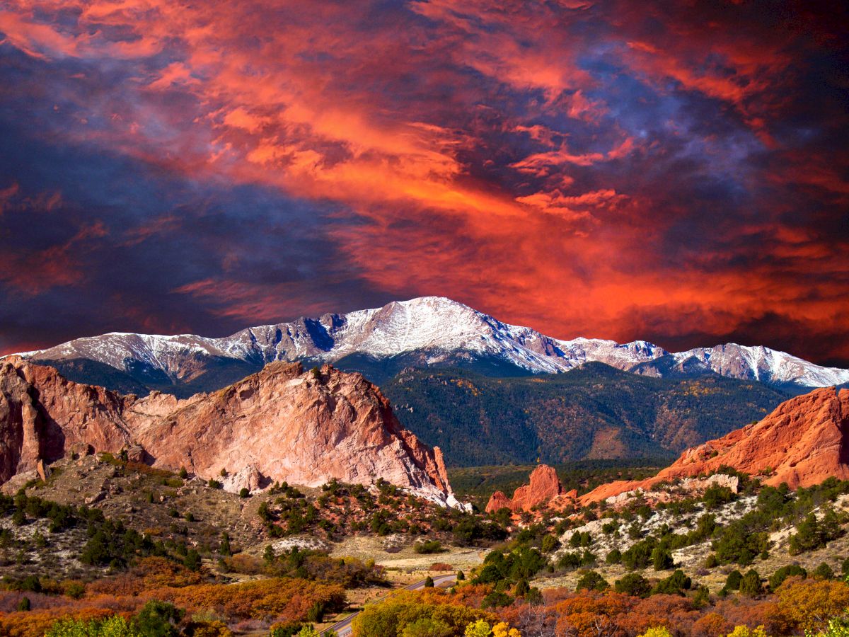 A vibrant sunset over snow-capped mountains with dramatic clouds and rocky terrain below.