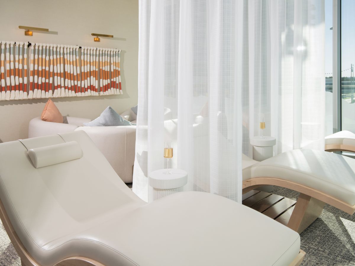 The image features modern white lounge chairs in a bright room with sheer curtains and decorative wall art for a relaxing ambiance.