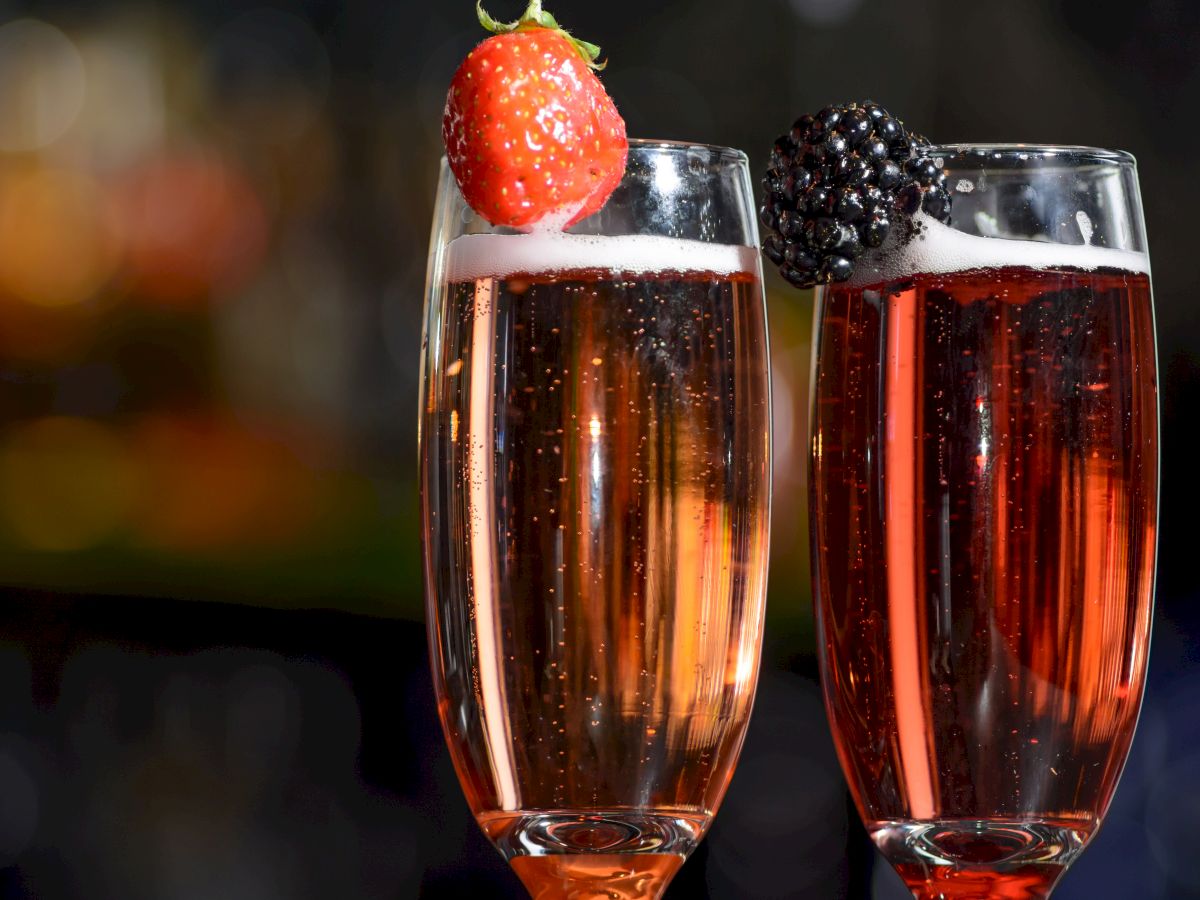 Two champagne flutes filled with a red sparkling beverage, each garnished with a strawberry and a blackberry.