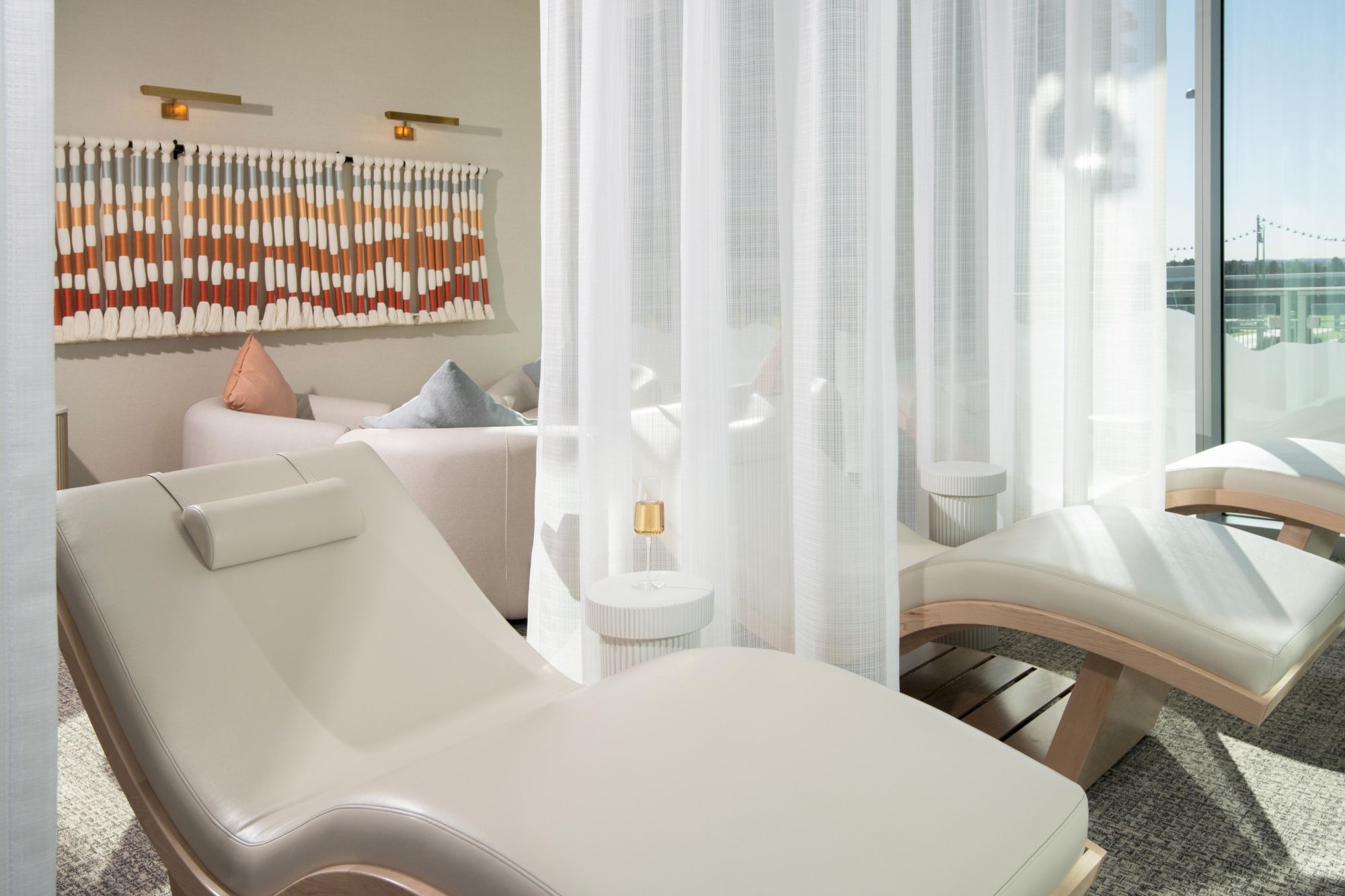 The image shows a relaxing spa room with lounge chairs, a curtain, wall art, and soft lighting.