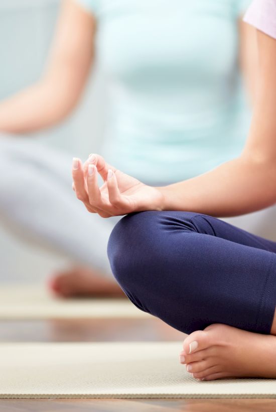 Two people are seated in a cross-legged position on yoga mats, meditating with hands in mudras.