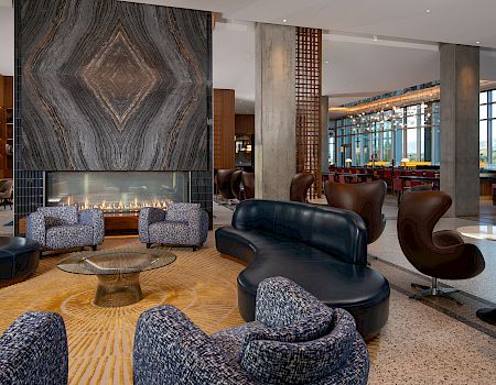 A modern lounge area with patterned chairs, a sculptural sofa, a large stone fireplace, and open spaces featuring natural light and chic decor.