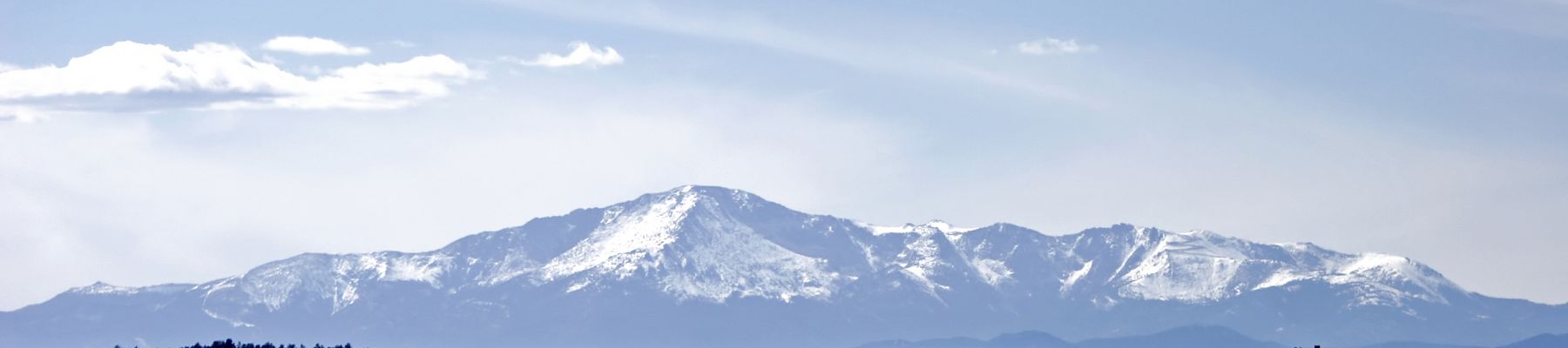 The image shows a snow-capped mountain range under a clear blue sky, with a flat grassy field in the foreground.