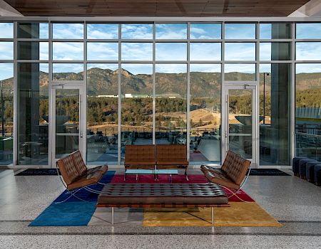 Modern room with large windows, mountain view, and mid-century furniture on a colorful rug.