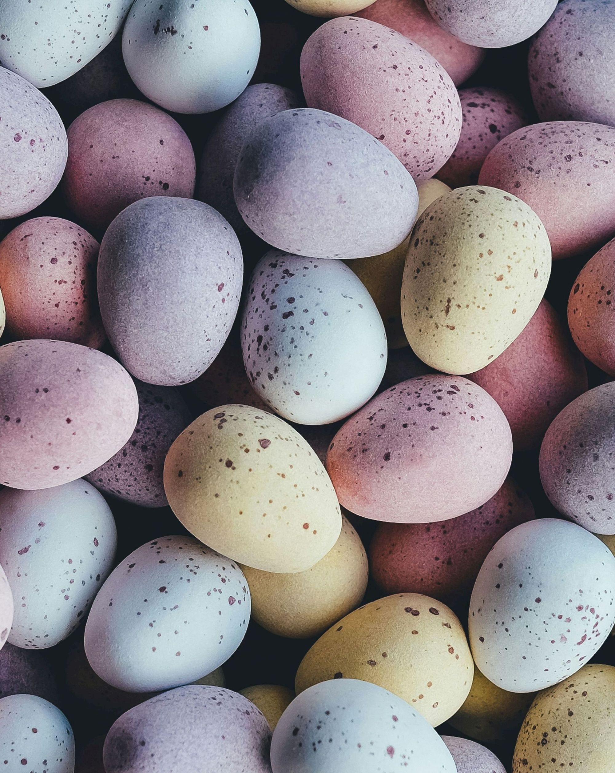 A collection of pastel-colored eggs with speckled patterns, arranged closely together.