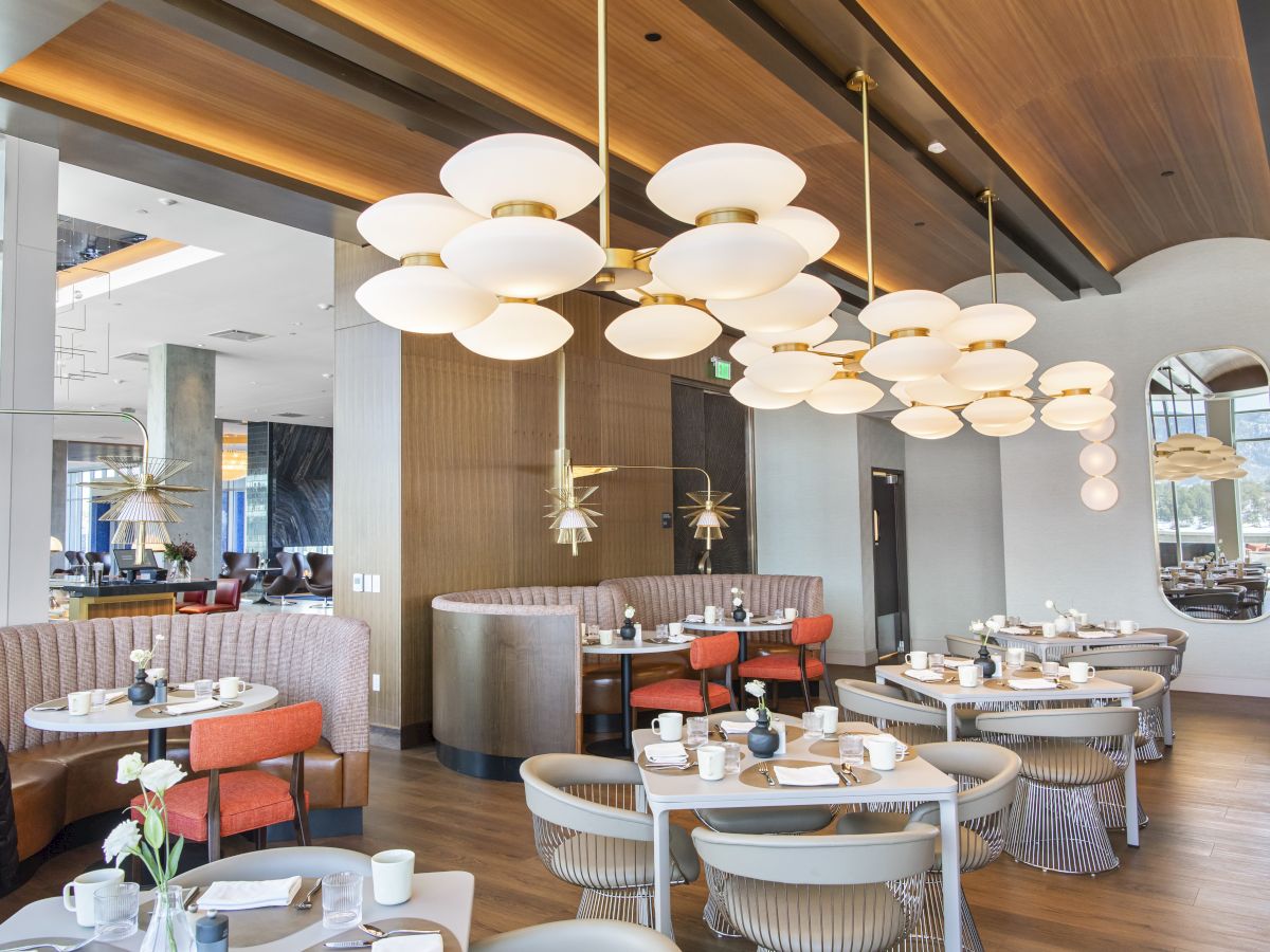 The image shows a modern restaurant interior with elegant lighting, tables set with dishes, and a warm, inviting atmosphere.