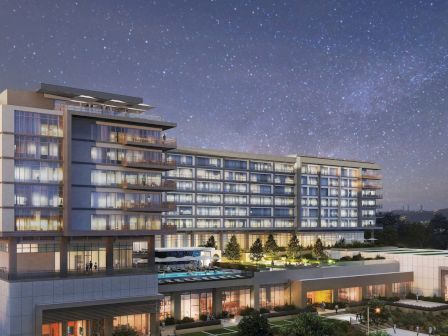 A modern multi-story building with illuminated windows under a starry sky, surrounded by landscaped greenery and pathways.