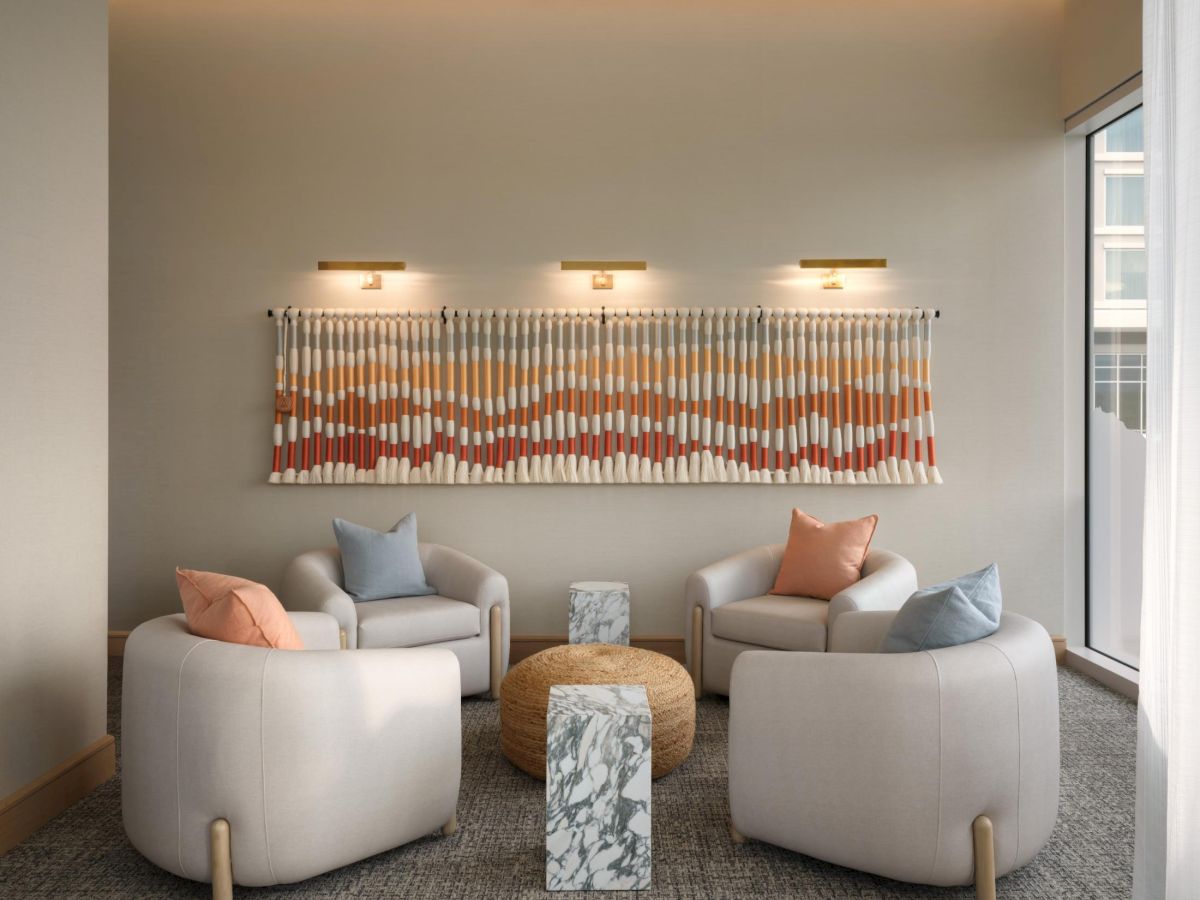 A modern lobby seating area with two curved light-gray chairs facing each other, a pair of peach and gray cushions, a patterned abstract wall art, a marble side table, and soft ambient lighting, ending with a period.
