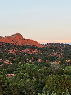 A landscape featuring red rock formations and greenery under a clear sky at sunset.