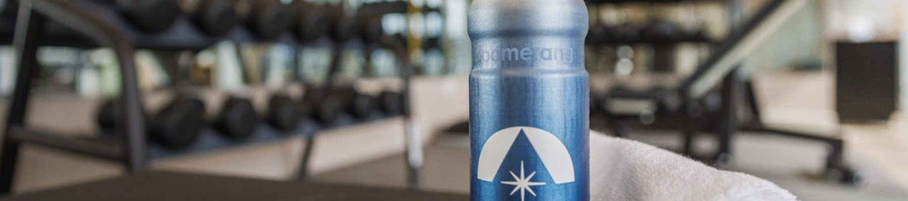 A bottle of water and a rolled towel on a table in a gym setting with exercise equipment in the background.