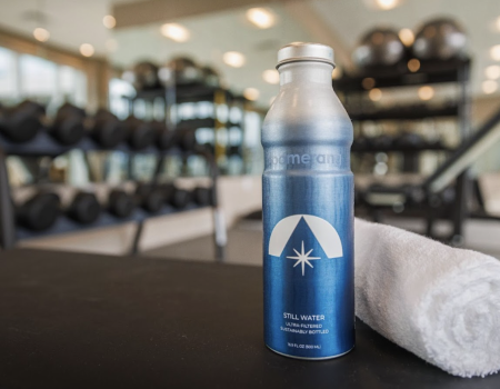 A bottle of water and a rolled towel on a table in a gym setting with exercise equipment in the background.