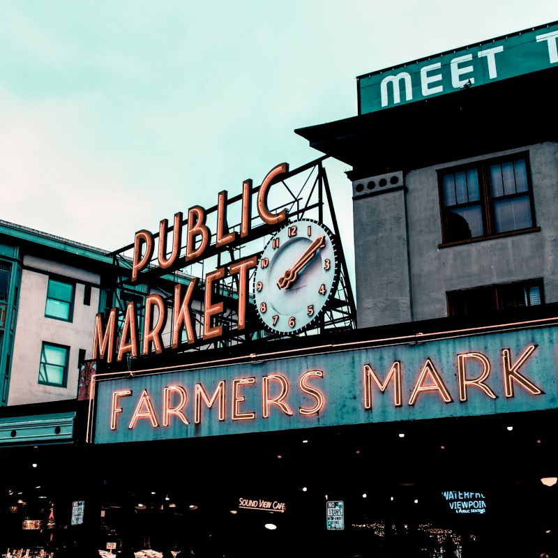 This image shows neon signs of a Public Market and Farmers Market with a clock in the center, likely the Pike Place Market in Seattle.