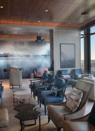 A modern lounge with leather chairs, large windows overlooking a waterfront, and a wall mural depicting a city skyline.
