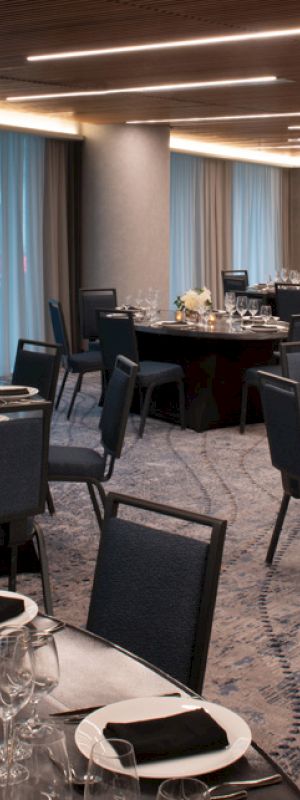 A well-lit banquet hall with round tables set up with black napkins, glassware, and flower centerpieces, ready for an event or dinner.