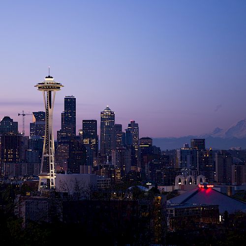 The image shows the Seattle skyline at dusk, featuring the Space Needle, various downtown buildings, and Mount Rainier in the background.