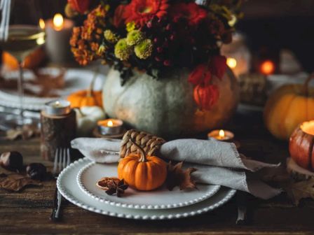 A cozy autumn table setting with candles, mini pumpkins, autumn leaves, and a floral centerpiece, creating a warm, festive atmosphere.