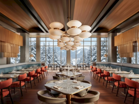 A modern restaurant interior with elegant tables, stylish lighting, and large windows revealing a snowy mountain view outside.