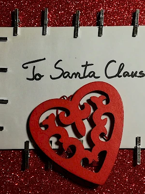 A card addressed to Santa Claus with a decorative red heart on a glittery background, framed by metal staples.